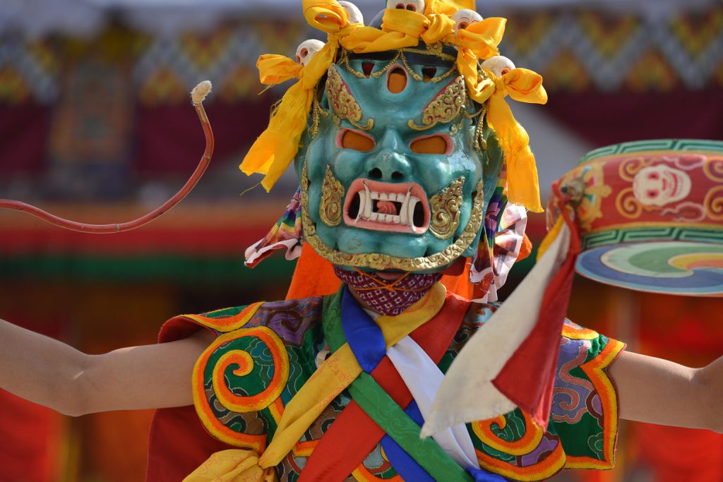 A monk performing a ritual cham dance wearing elaborate and colourful robes and a mask.