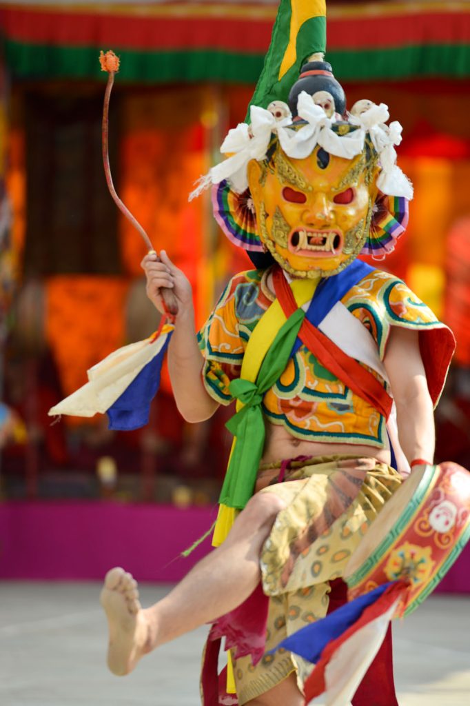 A monk performing a ritual cham dance wearing elaborate and colourful robes and a mask.