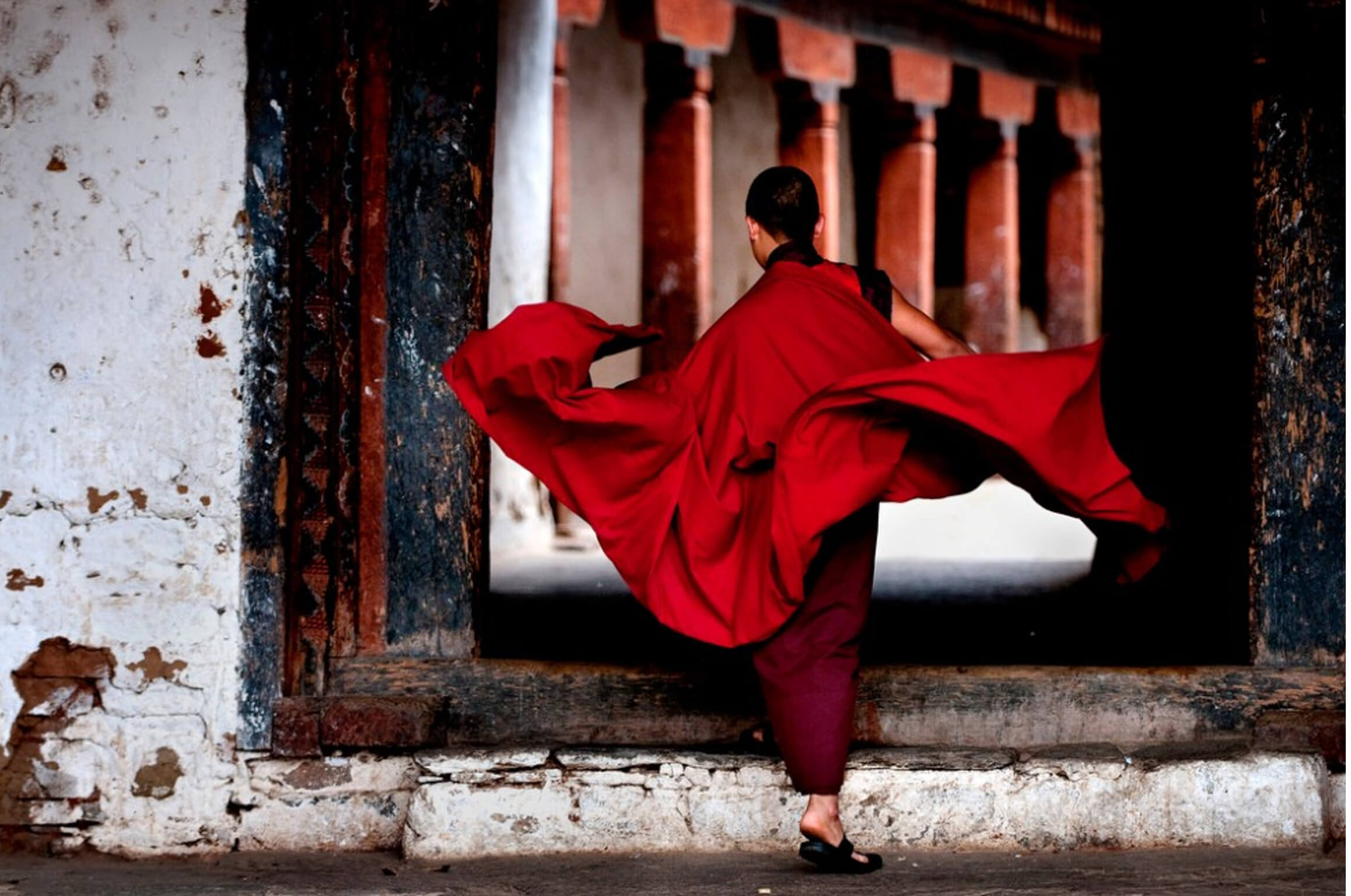 A monk in flowing red robes passing through a large doorway into a monastery.