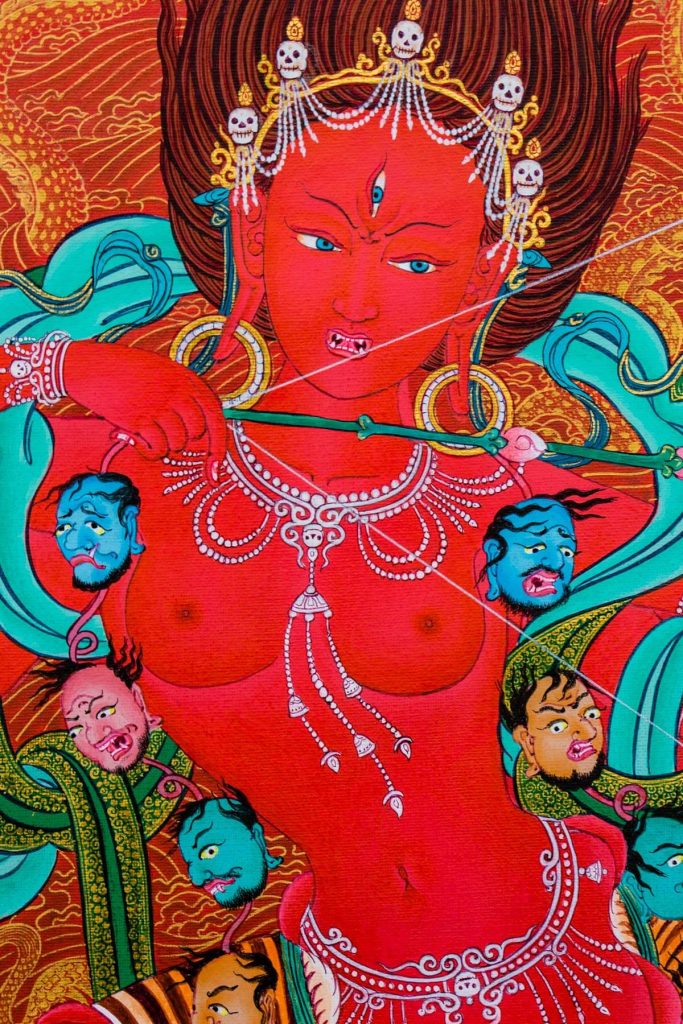 Kurukulla yogini depicted as red and blazing with flames, in dancing posture, holding in her hands the emblematic hooked knife and skull-cup of amrita, together representing the union of bliss and emptiness. Her ornaments of bone and jewels are similar to Vajrayogini’s, but she does not hold the khatvanga trident staff.