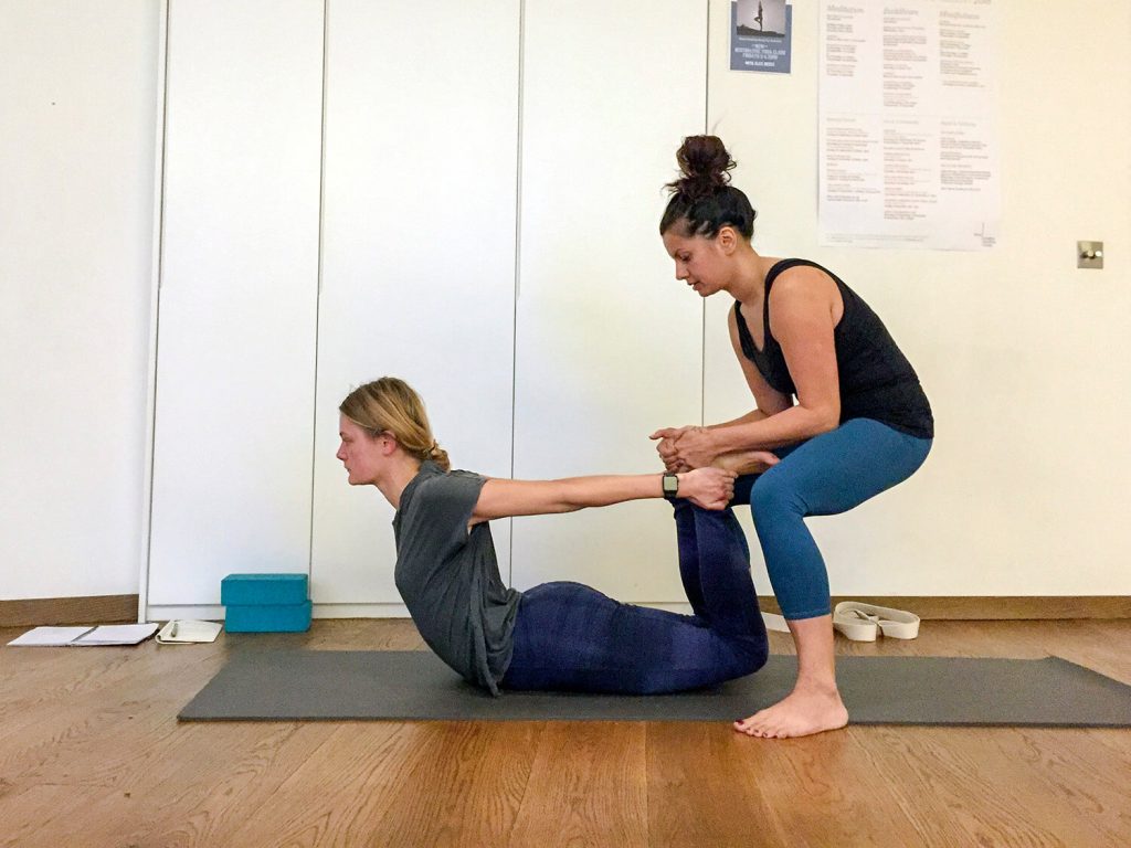 Rina Modi adjusts a fellow student on the Elton Yoga London Teacher Training course in bow pose (Dhanurasana).