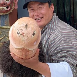 A bhutanese man holds a wang, an oversized sculpture of a phallus used for giving fertility blessings.